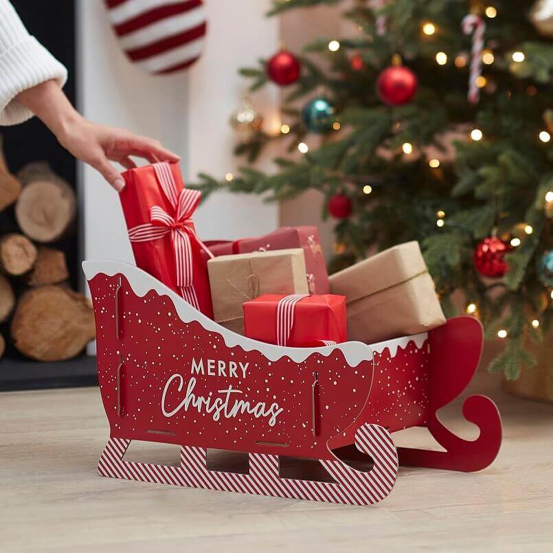 red sleigh Christmas decoration,placing gifts in sleigh Christmas decoration,creative Christmas tree decorating ideas,holiday gifts as decorations,holiday decor in red color,